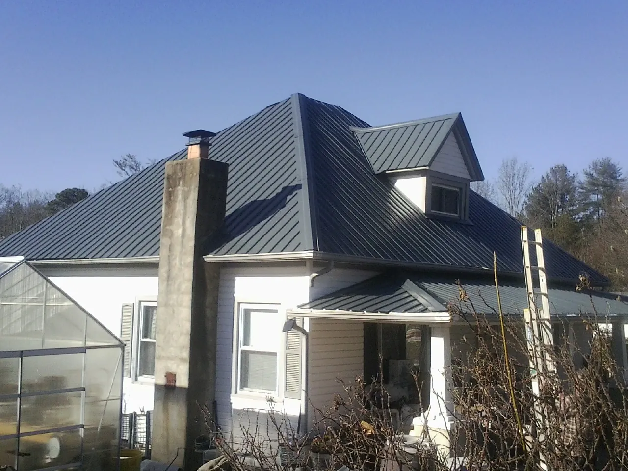 Dark blue standing seam metal roof on a white farmhouse with dormer — Slate & Tile Roof Repair by Roofing Brothers in Green Valley Lake