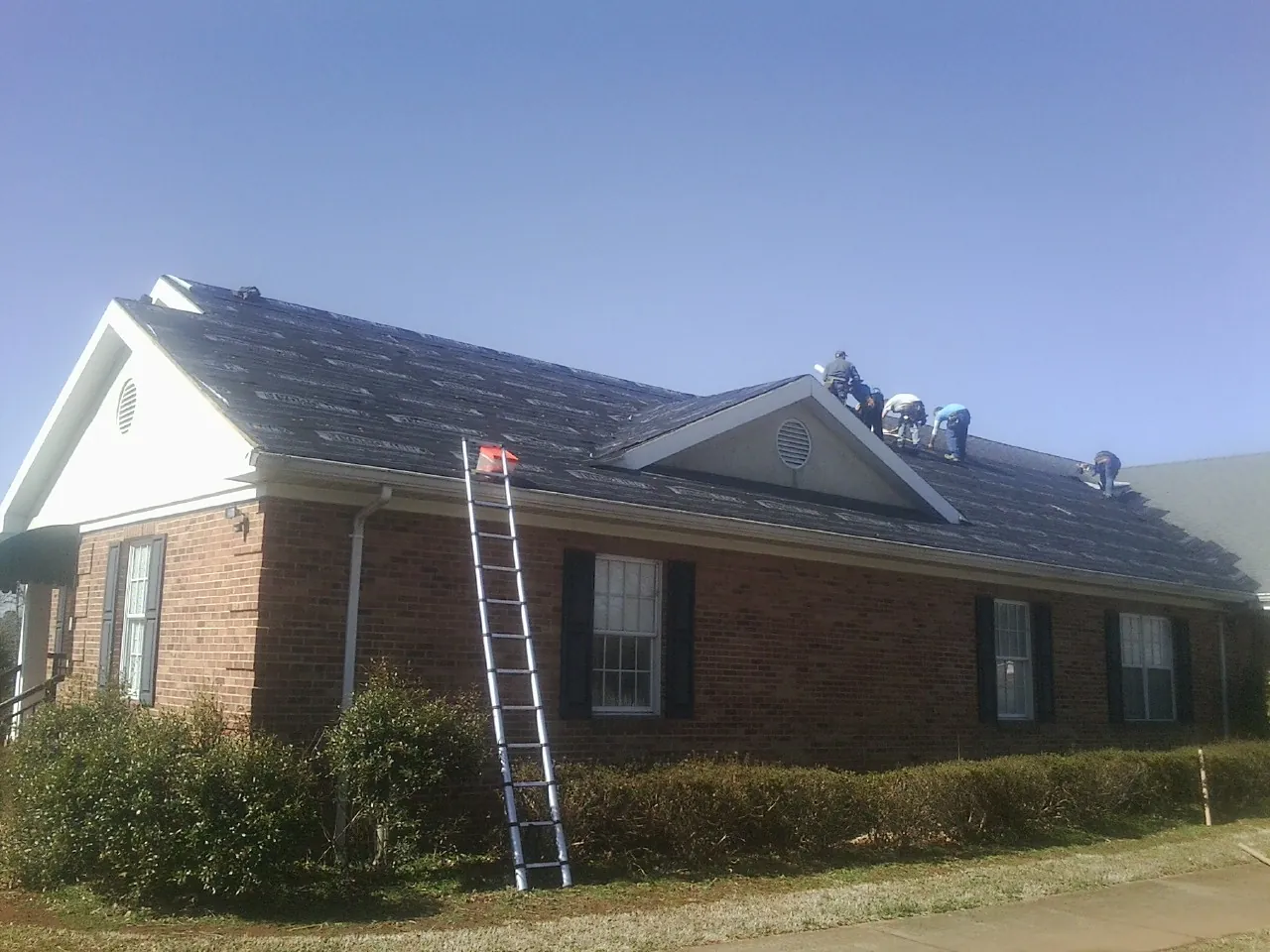 Crew tearing shingles off a brick ranch roof with a ladder set — Emergency Roof Repair work by our crew in Green Valley Lake