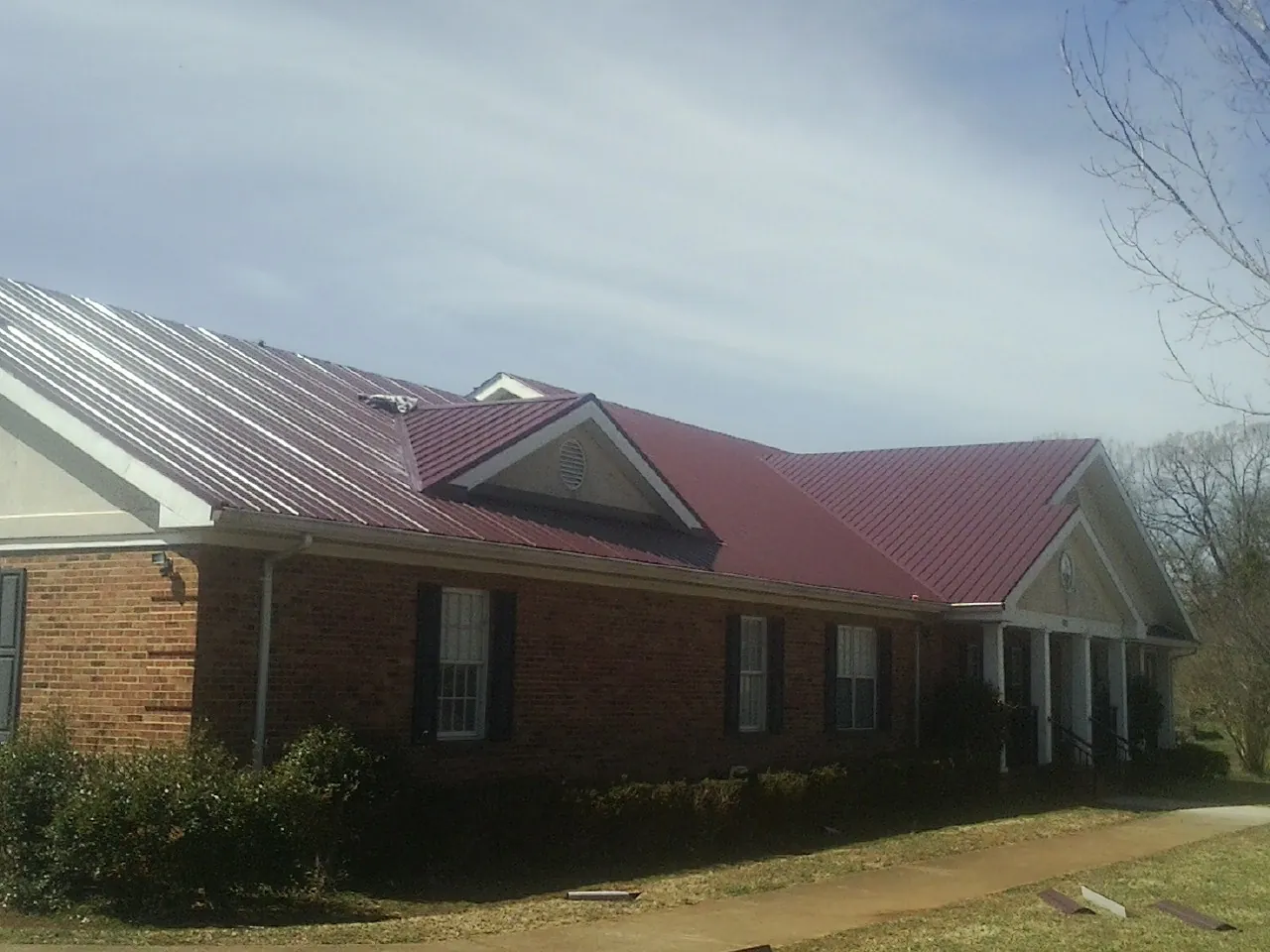 Red metal roof with gabled entries on a long brick building, from a Hail Damage Roof Repair job in Green Valley Lake