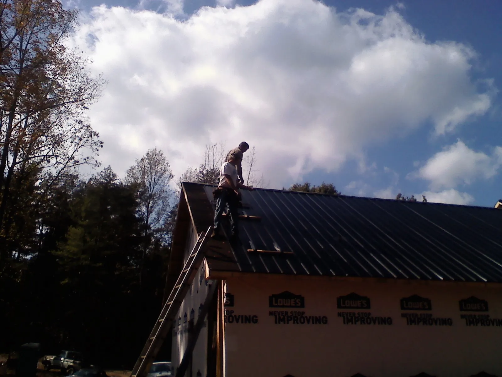 Roofer fastening dark metal panels high against a cloudy sky, from a Roof Inspection job in Green Valley Lake