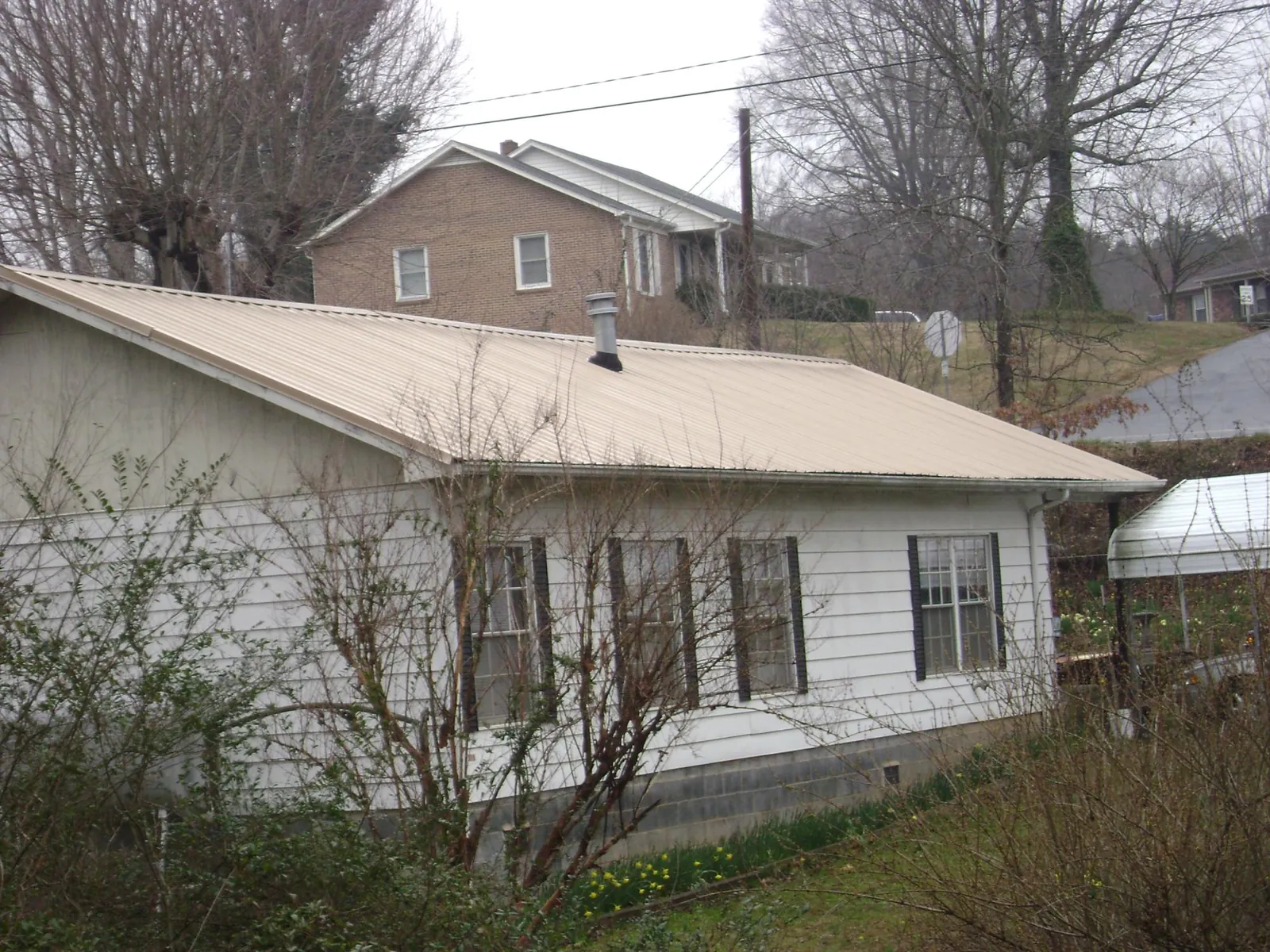 Tan metal roof on a white sided house set into a hillside — Commercial Roofing by Roofing Brothers in Green Valley Lake